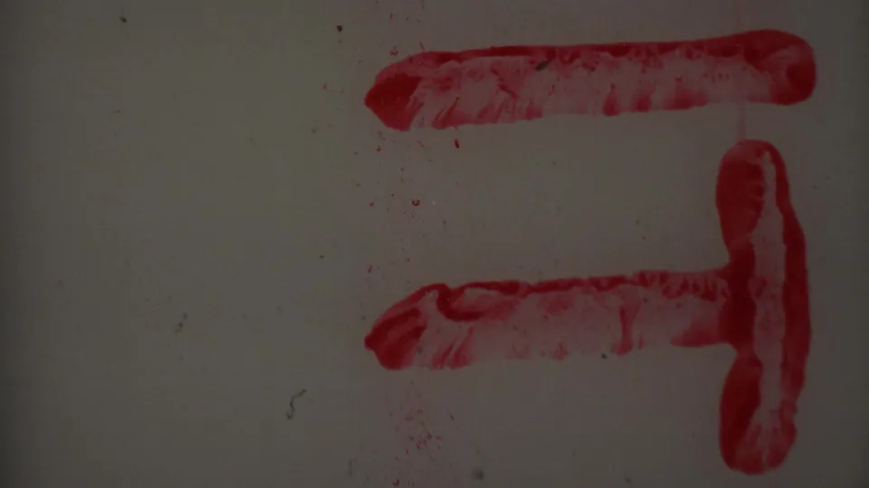 Close-up 1969 8mm frame showing red smeared horizontal and vertical strokes on a pale gray surface, with dust, scratches, and dark exposure.
