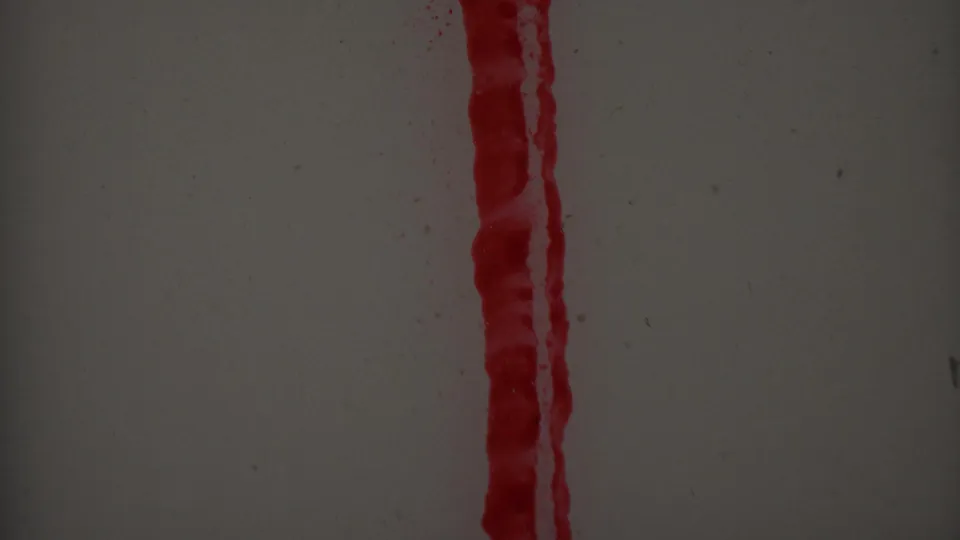 Close-up frame with a tall red vertical streak at the right edge and partial red smeared marks on a pale gray surface, recorded with visible 8mm grain.