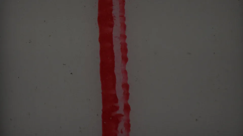 Close-up 1969 8mm frame centered on a thick red vertical smear against a pale gray field, with scratches, specks, and muted exposure.