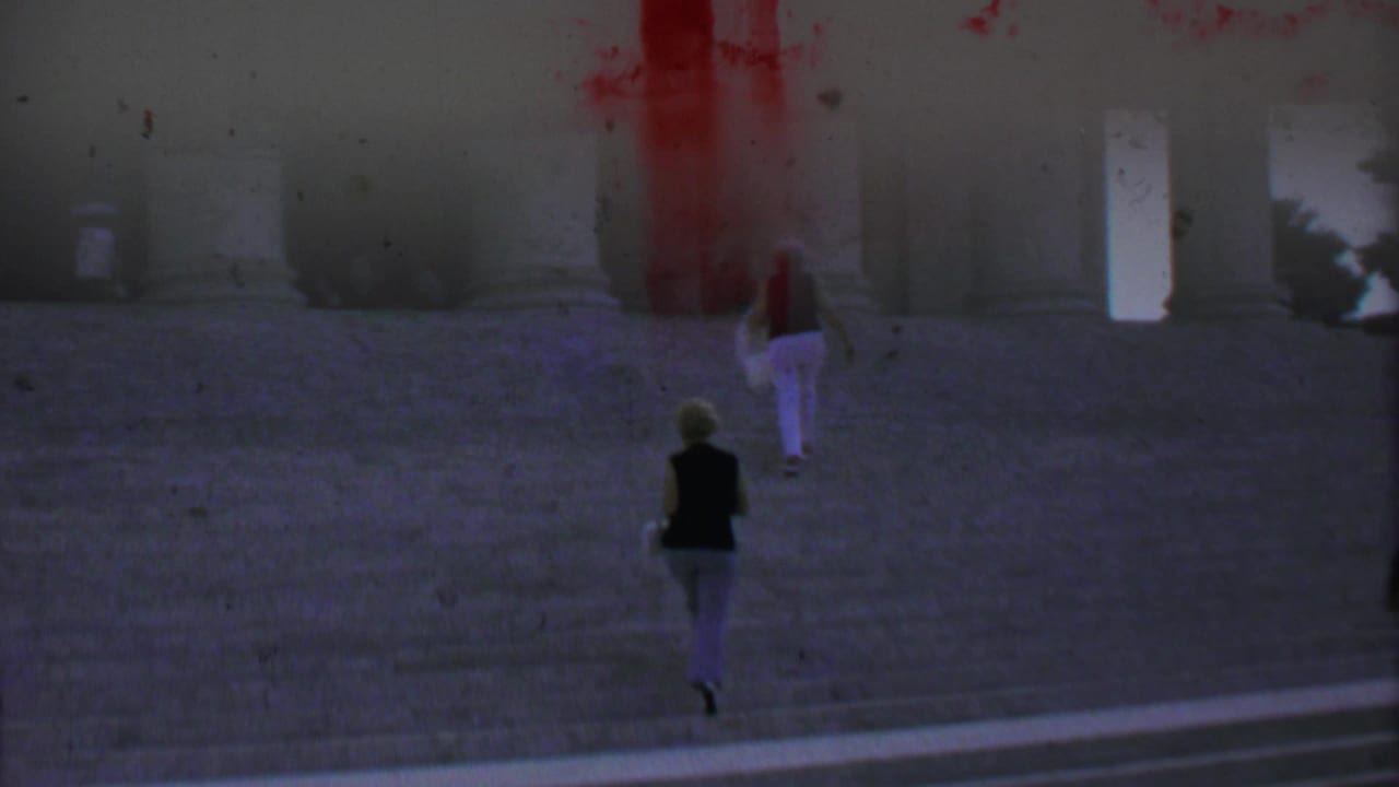 1969 home-movie frame from Washington DC showing two women ascending wide stone steps toward a neoclassical monument with massive columns.
