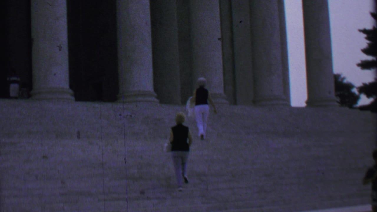Two women continue up the monument steps below tall columns.