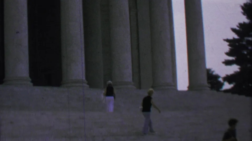 Final frame shows two women separated on the broad steps of a Washington DC monument, with columns, a dark entry bay, tree branches, and a passing figure at the lower edge.
