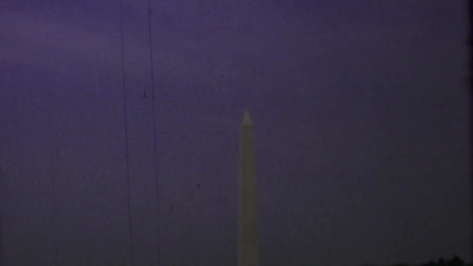 Washington Monument in Washington, DC, faintly lit against a deep purple twilight sky in 1969 8mm home-movie footage.
