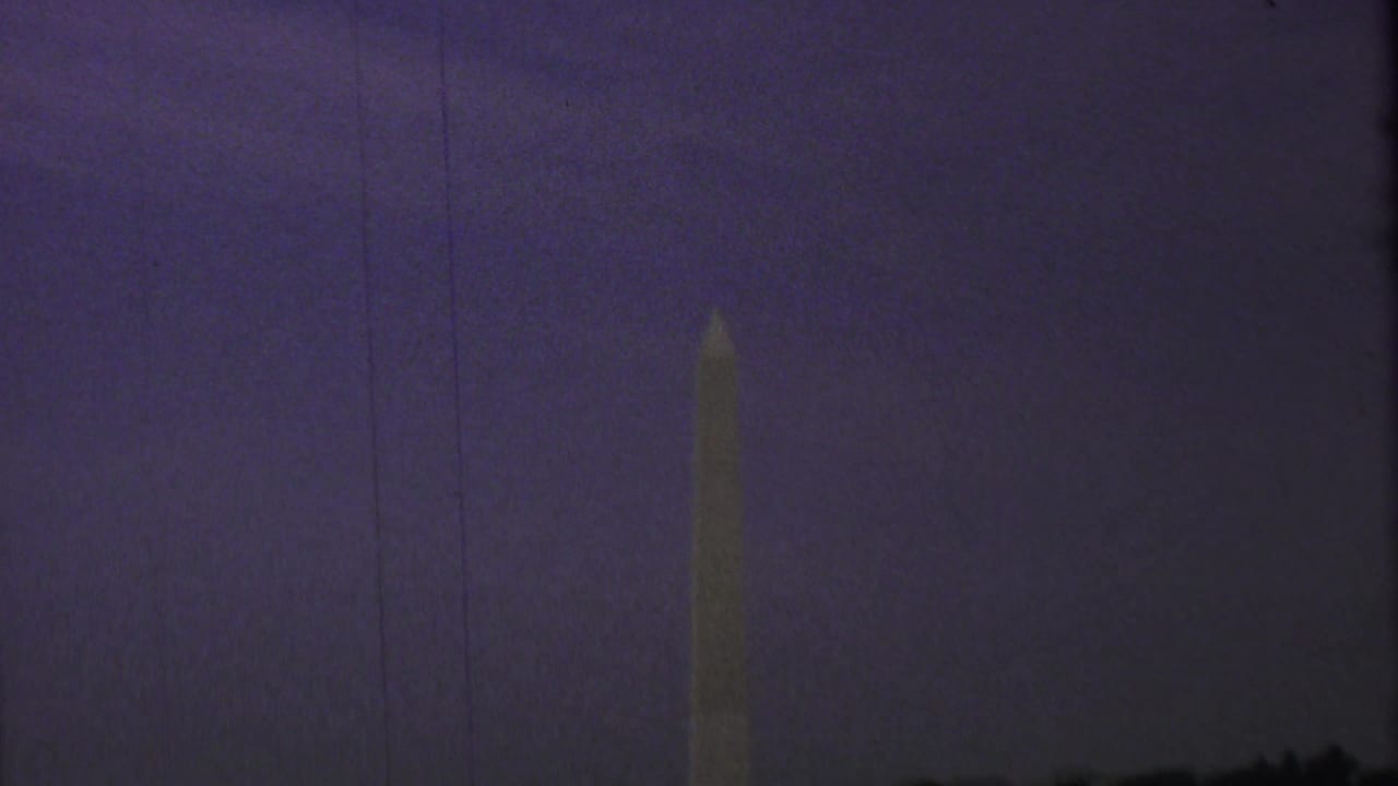 Dim 1969 8mm view of the Washington Monument standing against a purple evening sky with visible vertical film wear.