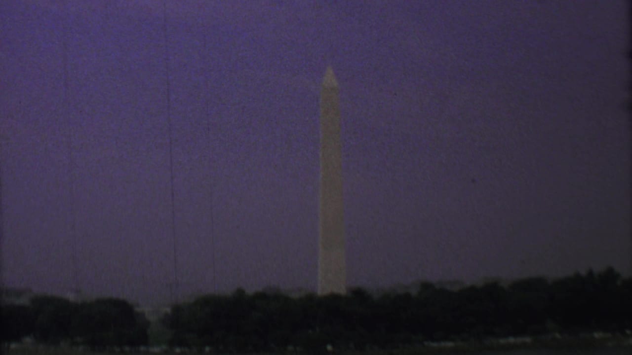 1969 8mm home-movie frame of the Washington Monument in Washington, D.C., viewed from across water with a silhouetted tree line at dusk.