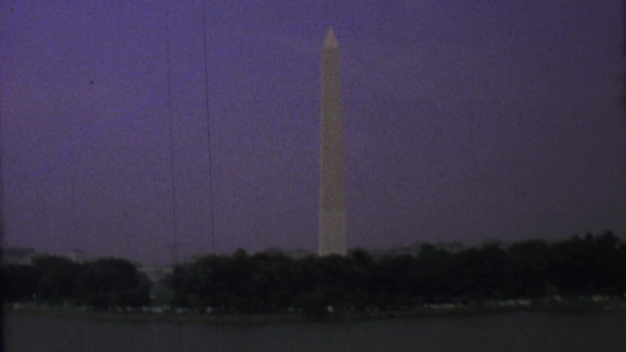 Washington Monument stands above trees with water in the foreground.