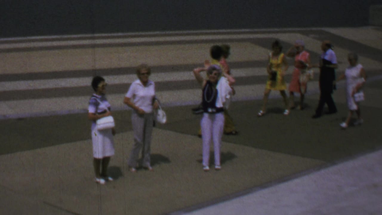 1969 Washington, DC home-movie frame showing several tourists, including Black visitors, standing and looking around on a broad concrete plaza near the Washington Monument grounds.