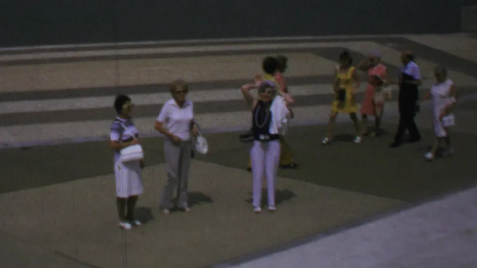 1969 Washington, DC home-movie frame showing several tourists, including Black visitors, standing and looking around on a broad concrete plaza near the Washington Monument grounds.