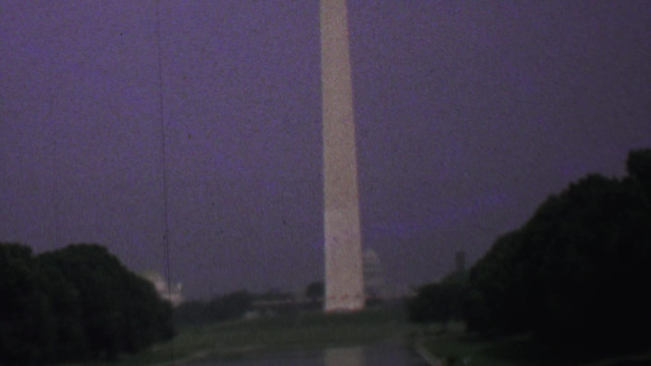 Closer view of the Washington Monument beside trees and the Reflecting Pool.