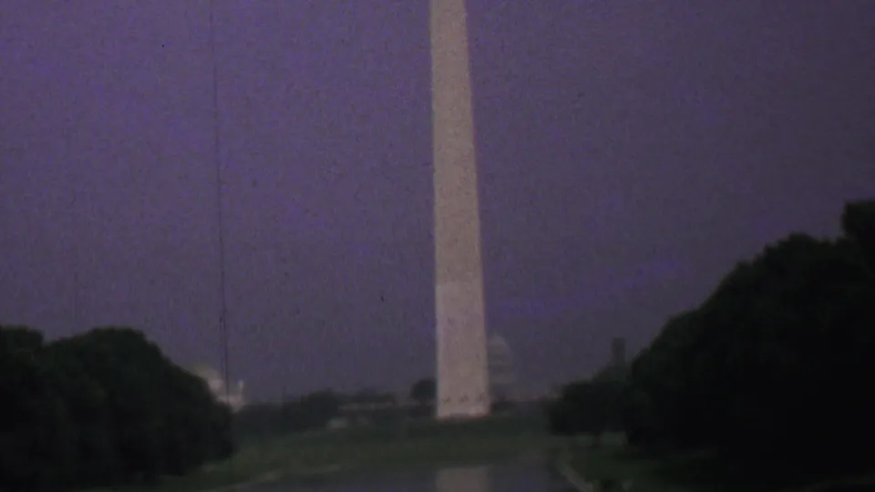 Closer 1969 Washington, DC home-movie view of the Washington Monument rising beside dark trees, with the Reflecting Pool and lawn visible below.