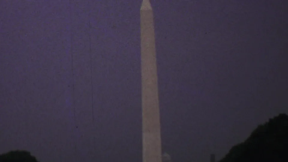 Zoomed 8mm frame of the Washington Monument in Washington, DC, with soft focus, visible film grain, and dark tree tops near the base.