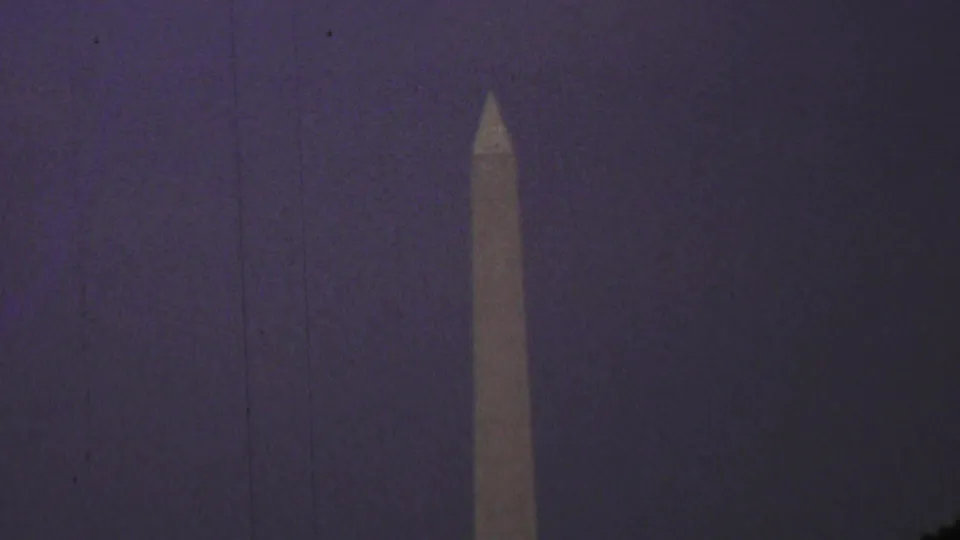Tight 1969 home-movie frame of the Washington Monument centered against a dark purple-blue sky, with park trees partly visible at the lower edge.
