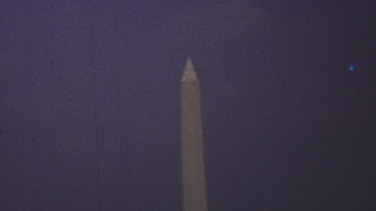 1969 8mm home-movie frame showing the Washington Monument rising into a dark, purple-tinted Washington, D.C. sky.