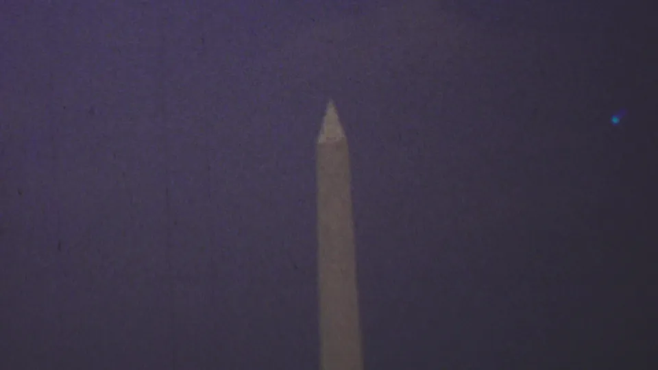 1969 8mm home-movie frame showing the Washington Monument rising into a dark, purple-tinted Washington, D.C. sky.