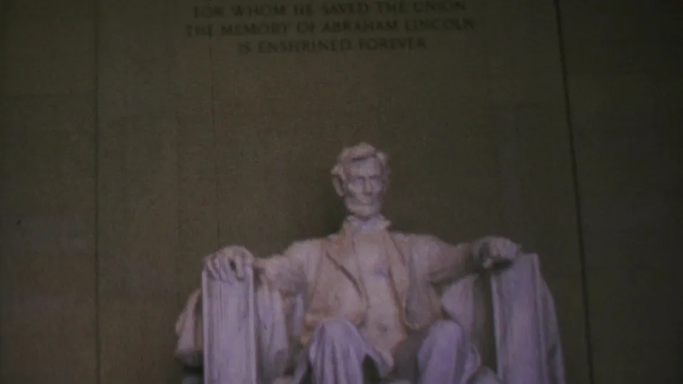 Visitor-shot 8mm frame of the seated Abraham Lincoln statue inside the Lincoln Memorial, with the engraved wall text faintly visible above.