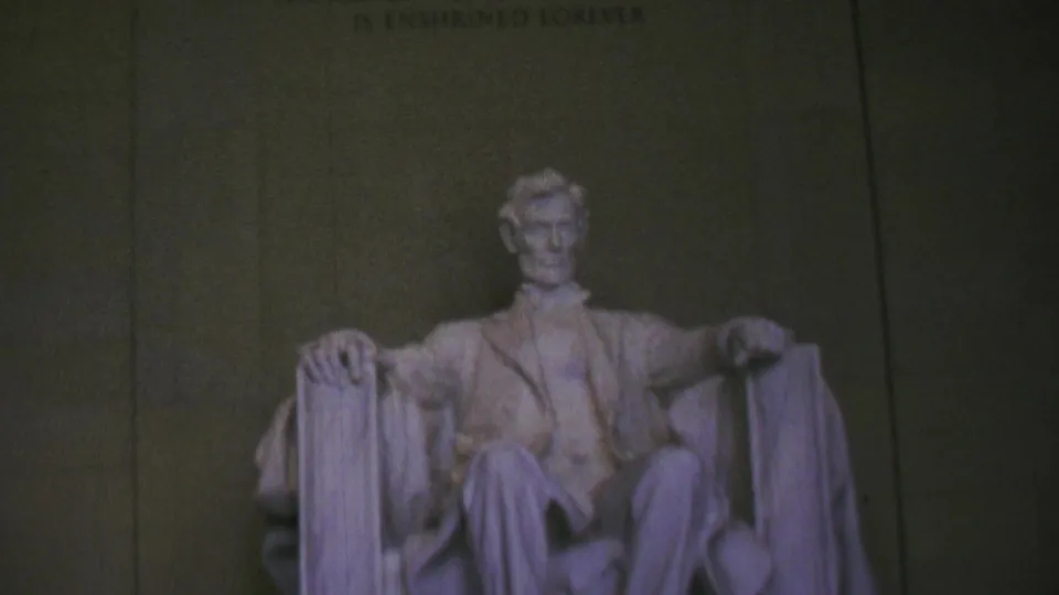 Soft-focus 1969 home-movie frame showing the seated Lincoln statue from inside the Lincoln Memorial, with the chamber wall rising behind it.