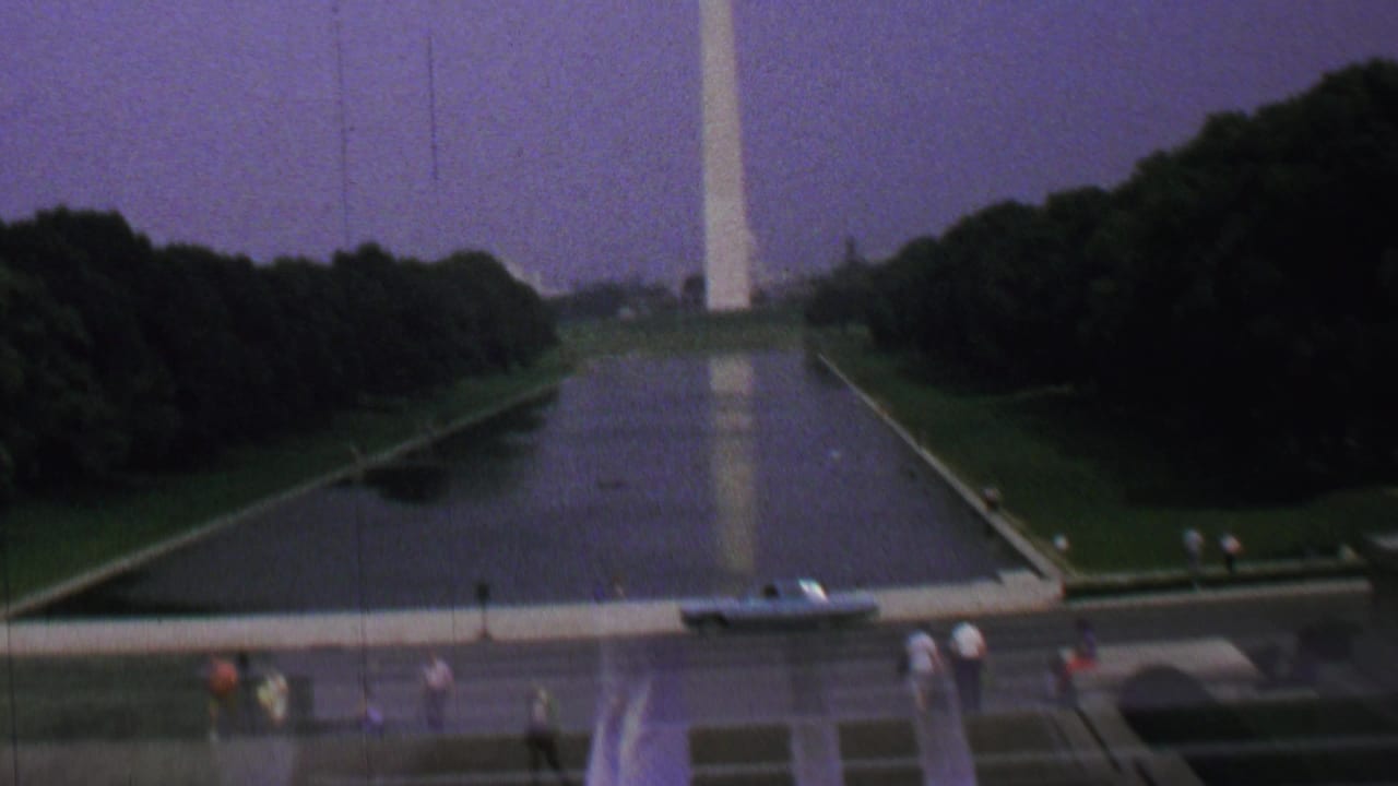 1960s 8mm view of the Washington, D.C. Reflecting Pool and Washington Monument, framed beside a dark engraved memorial wall and scattered tourists.