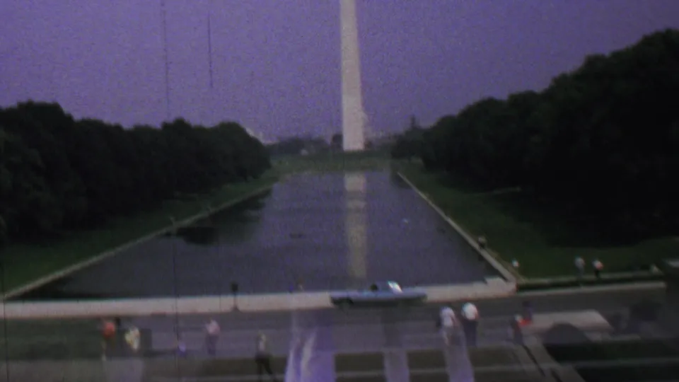 1960s 8mm view of the Washington, D.C. Reflecting Pool and Washington Monument, framed beside a dark engraved memorial wall and scattered tourists.