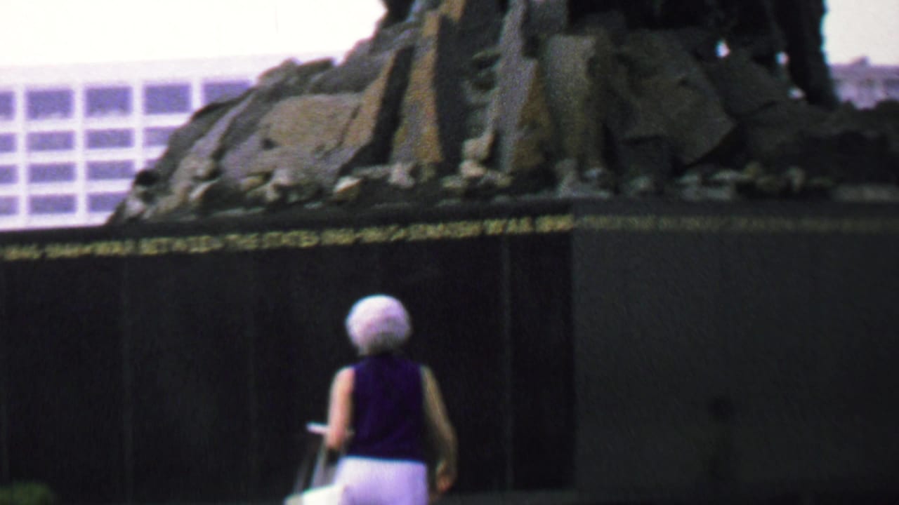 In supplied 1969 Washington DC home-movie footage, a woman with short white hair stands near the dark base of the Iwo Jima Memorial as part of the bronze sculpture rises above her.