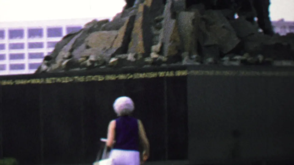 In supplied 1969 Washington DC home-movie footage, a woman with short white hair stands near the dark base of the Iwo Jima Memorial as part of the bronze sculpture rises above her.