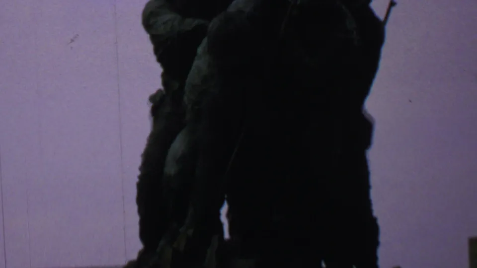 A tight upward view shows the Iwo Jima Memorial figures in heavy shadow against a pale sky, with film scratches and soft exposure visible in the 8mm scan.