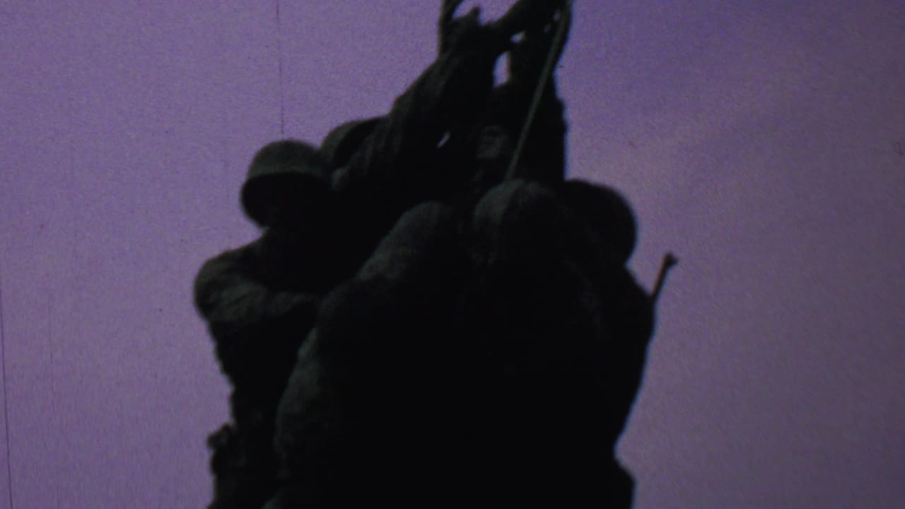 1969 8mm home-movie frame from Washington, DC showing the Iwo Jima Memorial figures in dark silhouette as they raise the flagpole against a purple-tinted sky.