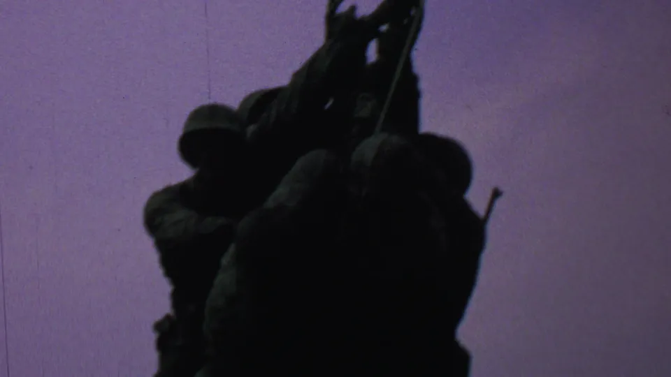 1969 8mm home-movie frame from Washington, DC showing the Iwo Jima Memorial figures in dark silhouette as they raise the flagpole against a purple-tinted sky.