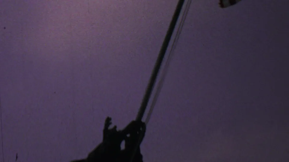 1969 8mm frame with the Iwo Jima Memorial flagpole crossing the composition and a lower silhouetted sculptural figure visible near the base of the frame.