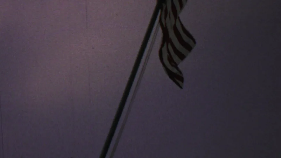 A closer angled view shows the American flag and pole in low light, with the fabric partially visible in silhouette against the purple dusk sky.