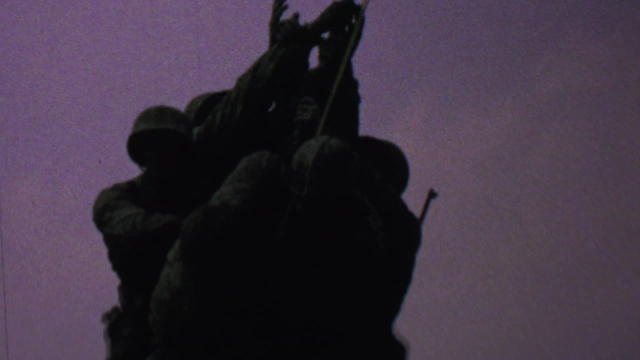 1969 Washington, DC home-movie frame showing the Iwo Jima Memorial sculpture in dark silhouette from a low angle against a purple twilight sky.