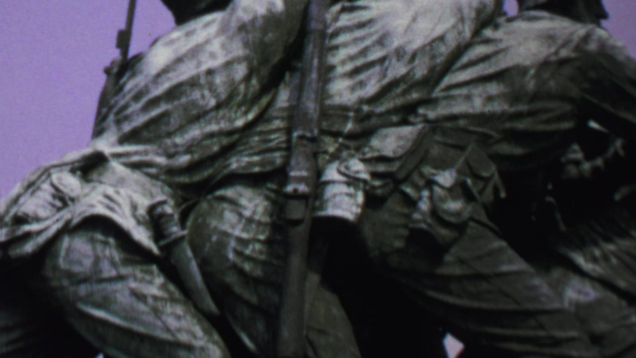 1969 Washington, DC home-movie frame showing a tight upward view of sculpted Marines on the Iwo Jima Memorial, with packs, a rifle, and bronze figures filling the frame.