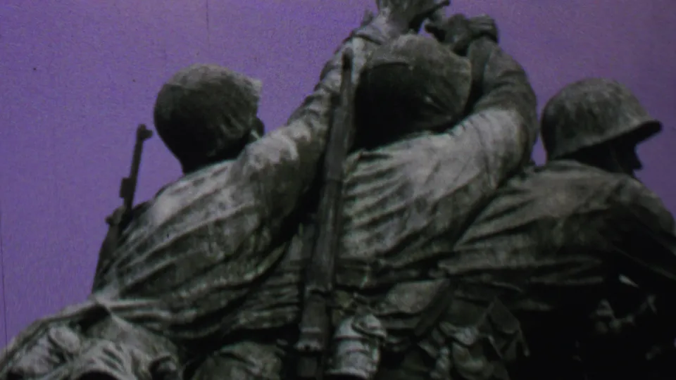 1969 Washington, DC home-movie frame showing the Iwo Jima Memorial from below, with bronze uniforms, packs, a helmeted figure, and the flagpole visible.