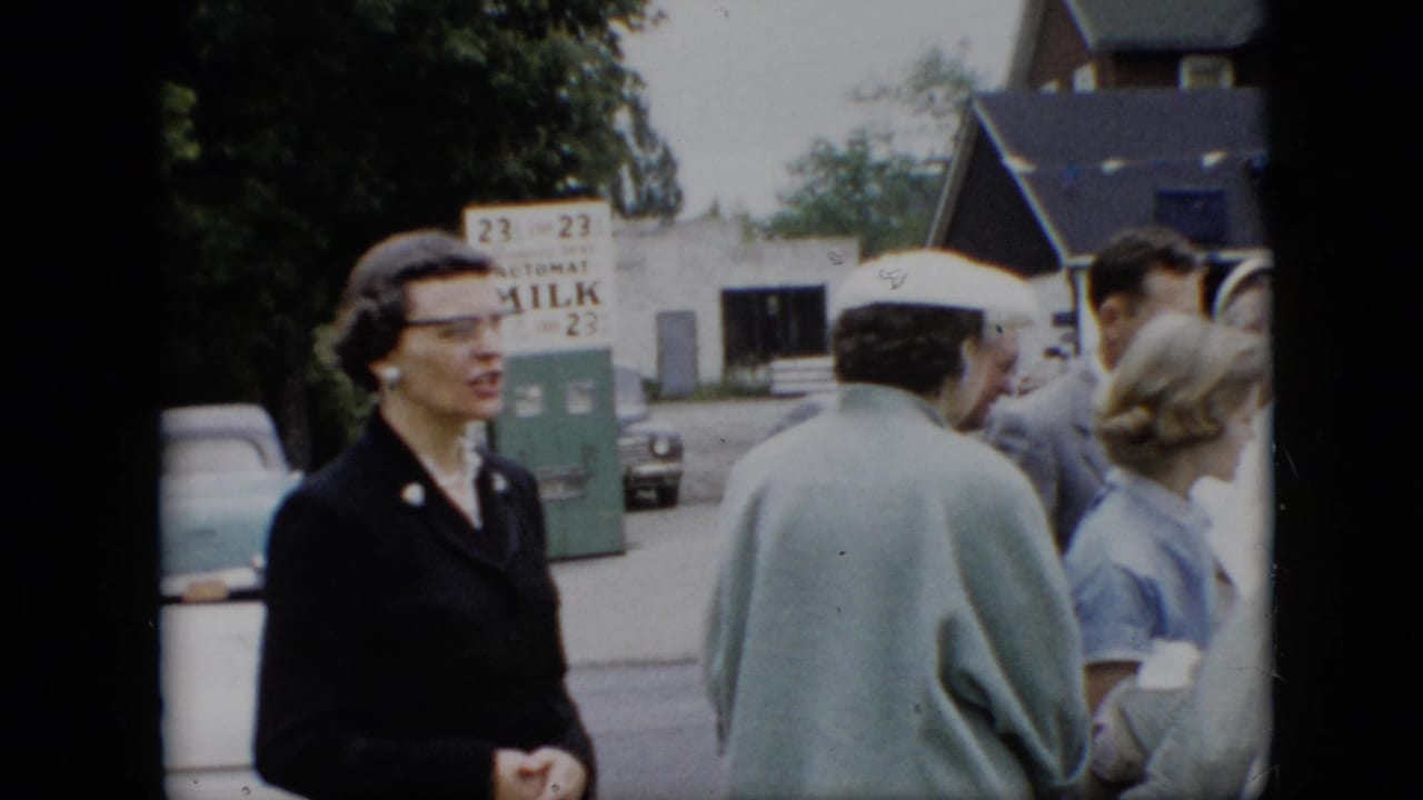 A woman in dark clothing stands near other adults with a milk sign in the background.