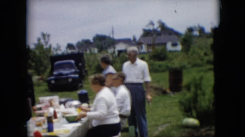The closing frame shows seated adults beside the picnic table and a standing man in a grassy Pennsylvania yard, with a dark car, shrubs, and houses beyond them.