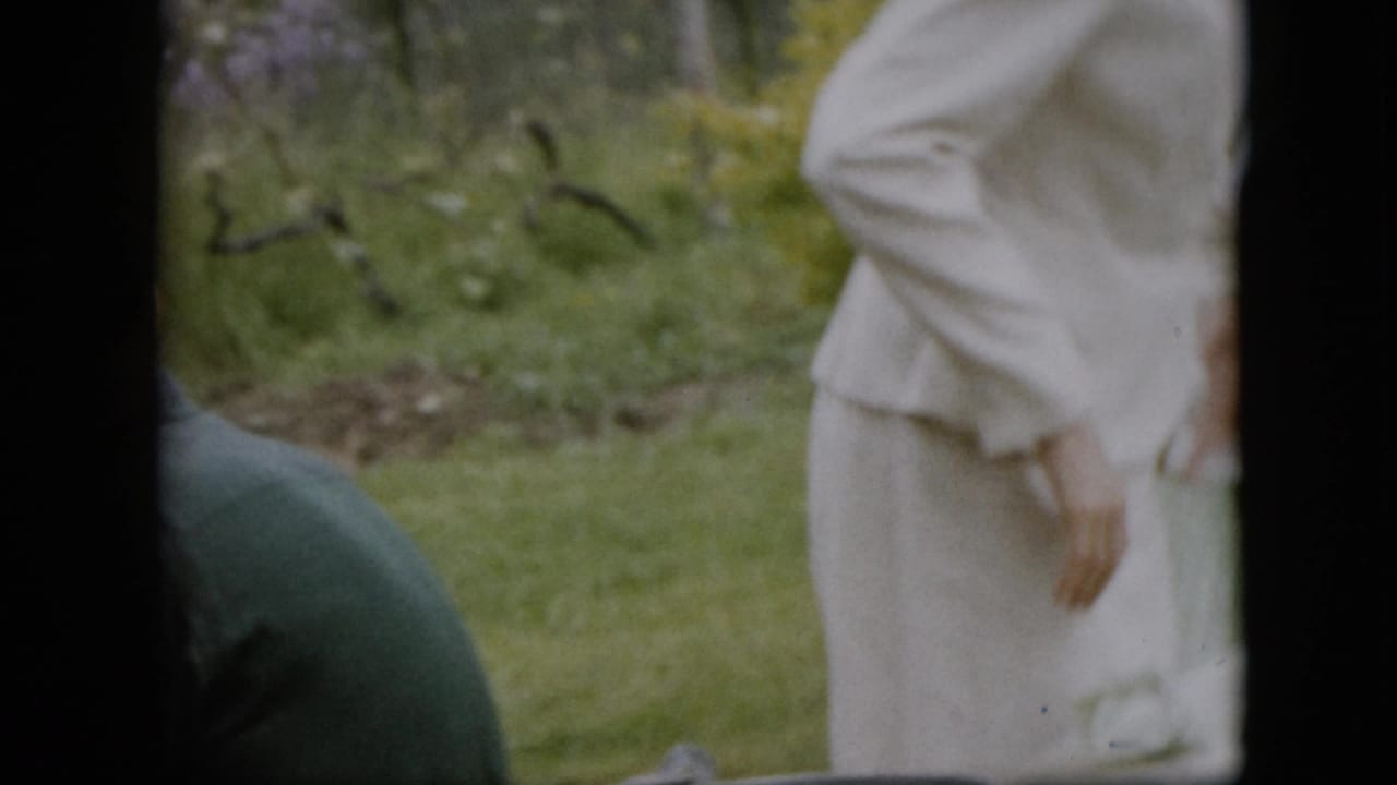 A white-clad adult stands in the foreground of a 1957 Pennsylvania outdoor gathering while another adult is partly visible lower in the frame on the lawn.