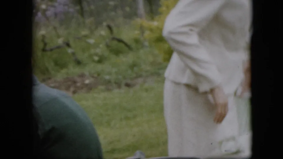 A white-clad adult stands in the foreground of a 1957 Pennsylvania outdoor gathering while another adult is partly visible lower in the frame on the lawn.