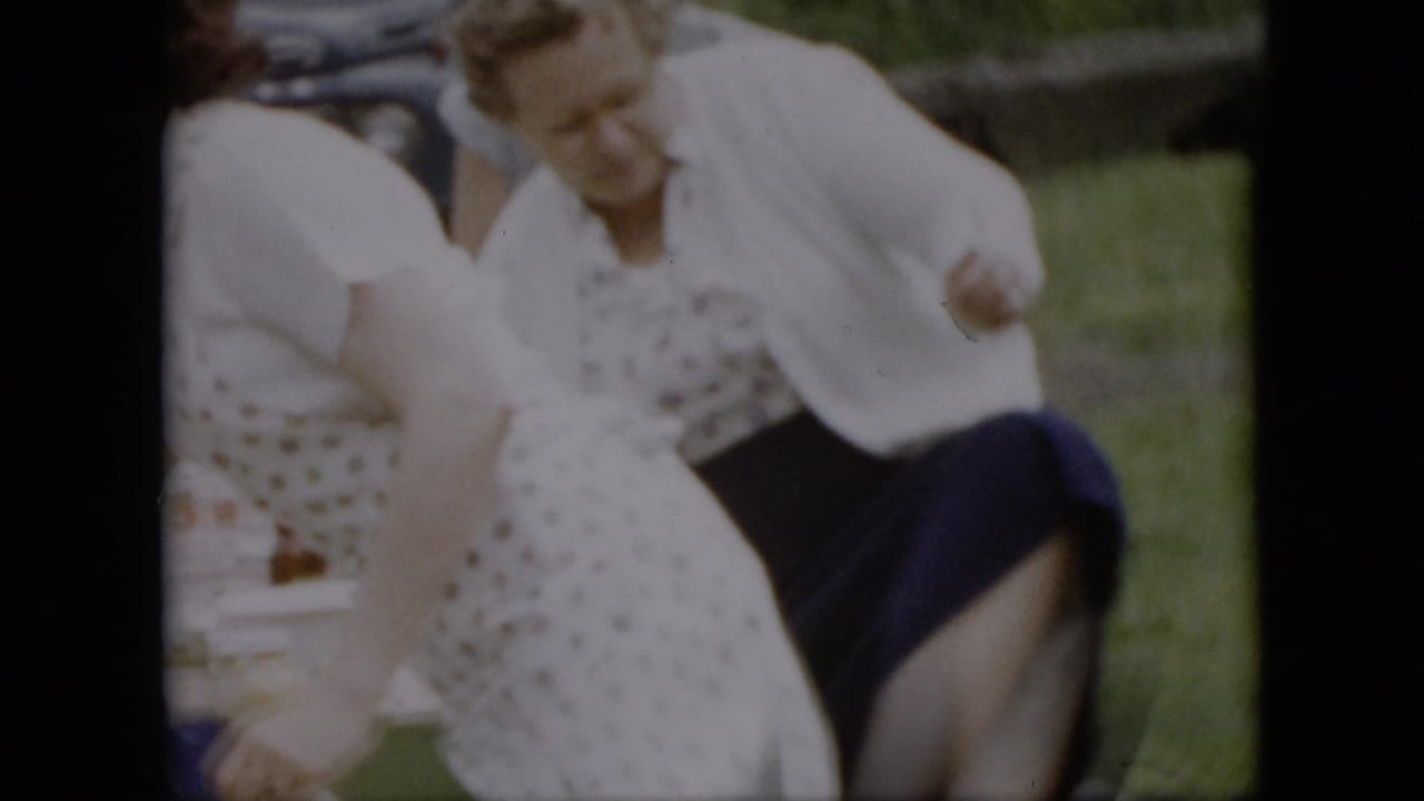 Women in aprons and skirts move around a picnic table with food items.