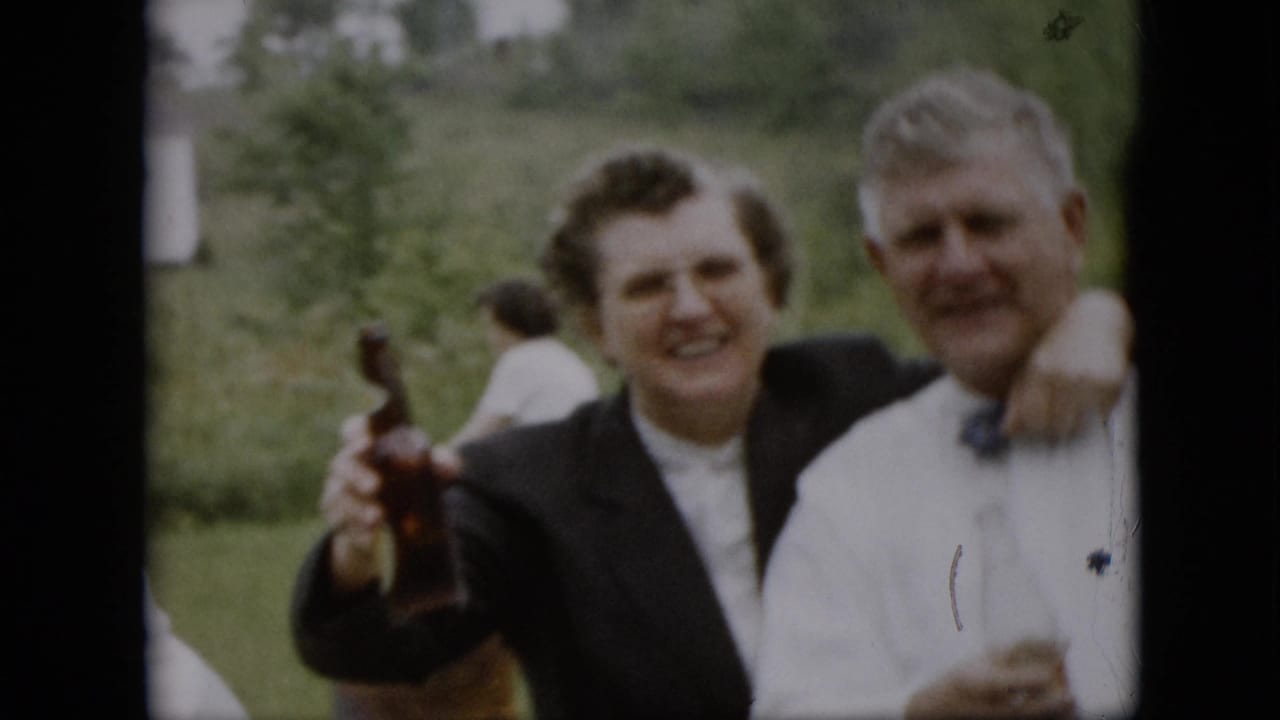 Smiling woman with a bottle stands beside a man in a white shirt and bow tie.