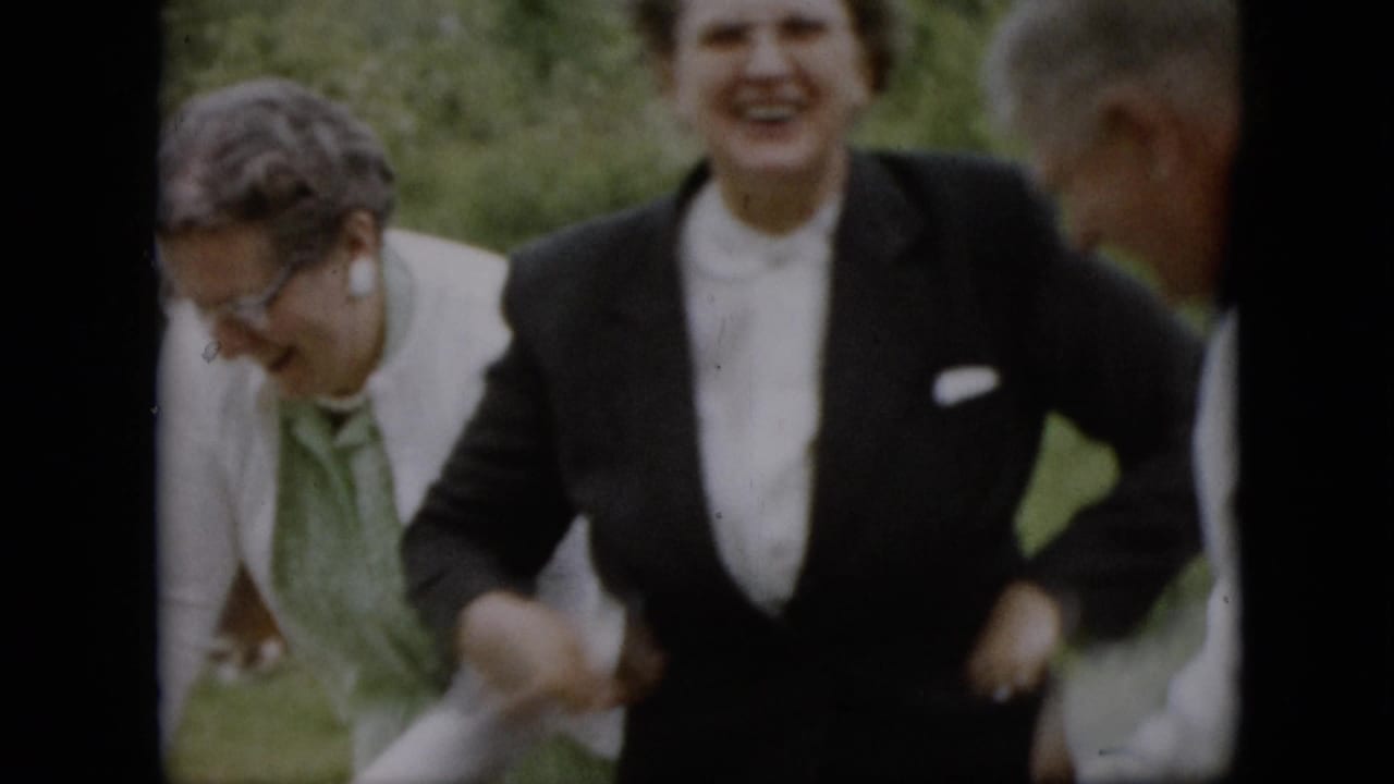 Two women laugh outdoors while another adult is partially visible nearby.
