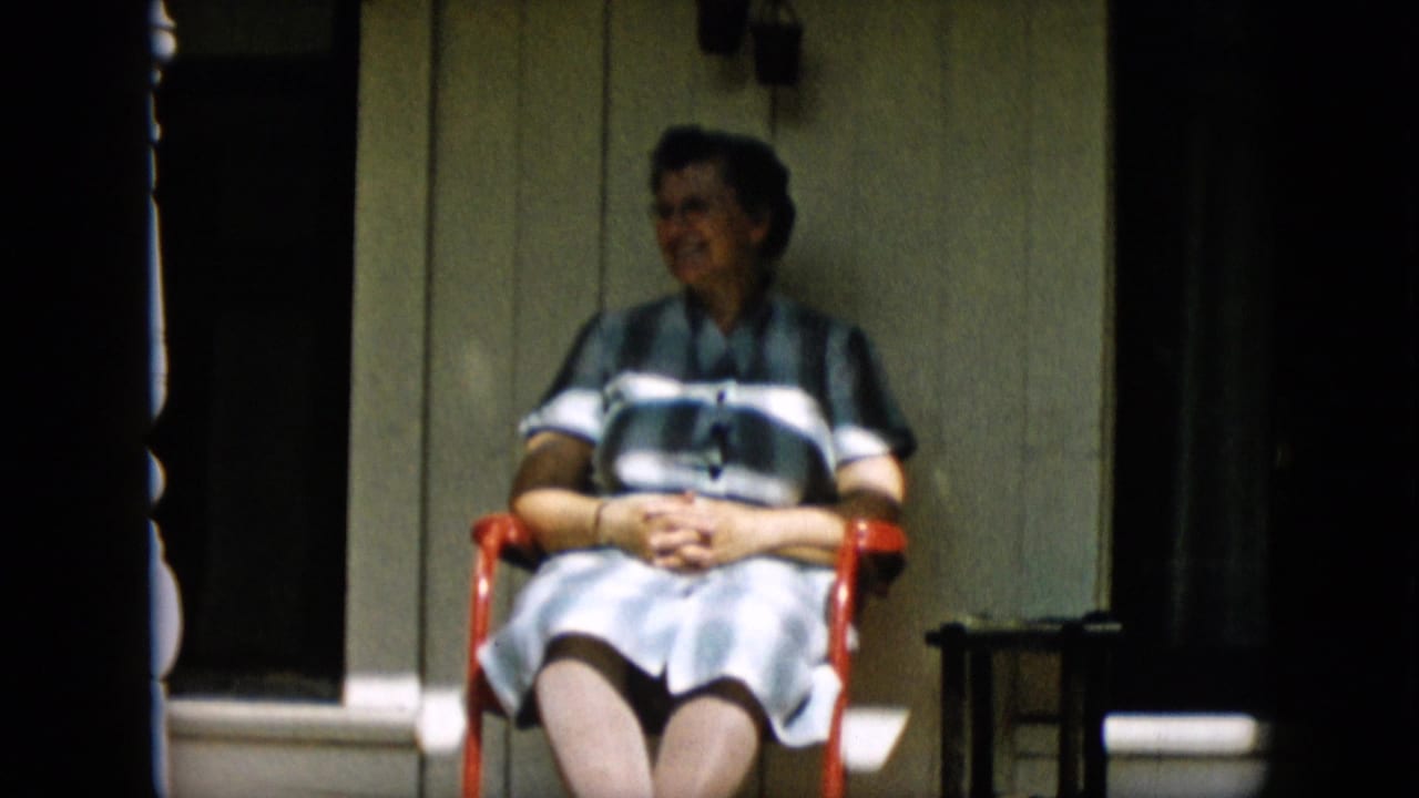 Woman seated in a red chair on a porch, smiling toward the side.