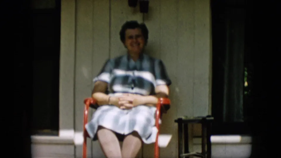 A softer frame shows the woman seated in the same porch position, her hands together and her face directed toward the camera in informal home-movie framing.