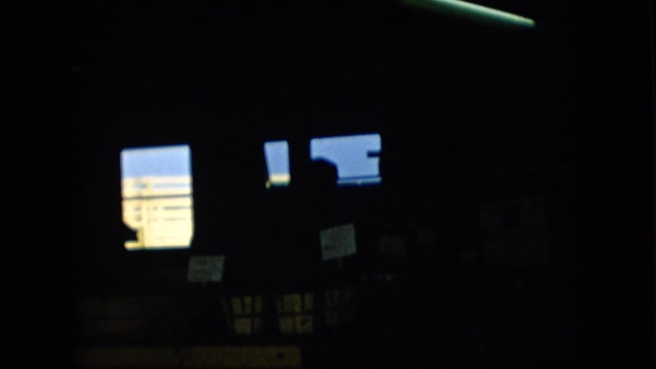Pennsylvania 1957 8mm frame showing a dim interior with blue-white window light, small posted signs, and a dark human silhouette near the right side.