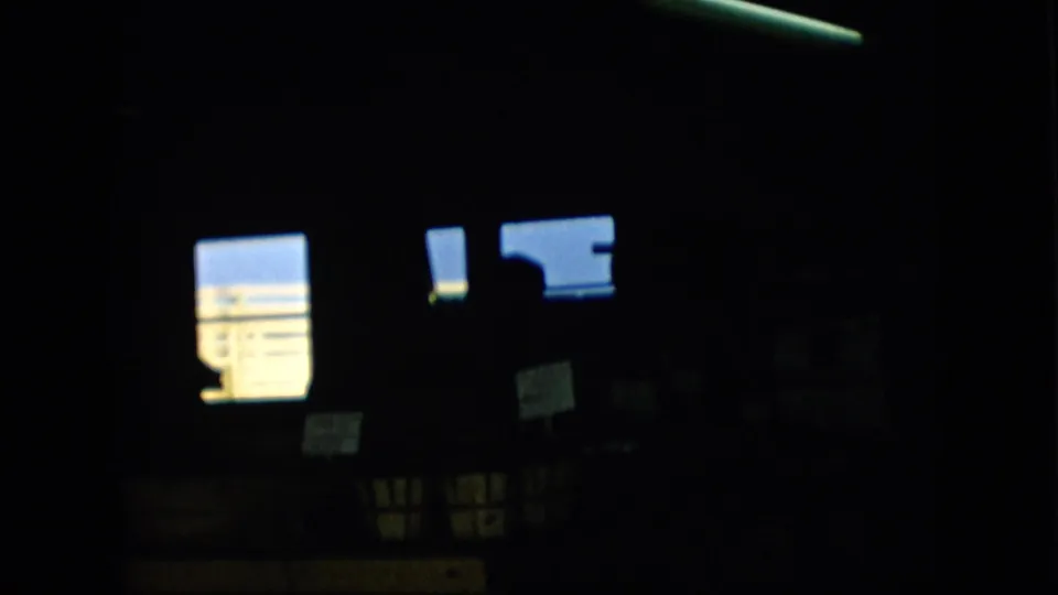 Pennsylvania 1957 8mm frame showing a dim interior with blue-white window light, small posted signs, and a dark human silhouette near the right side.