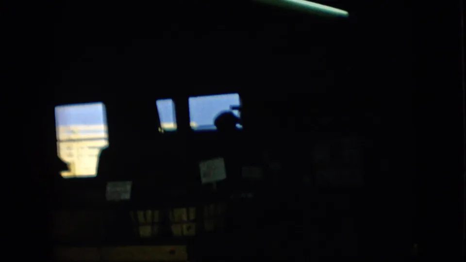 Pennsylvania 1957 8mm frame with a nearly black interior, bright window panels, small signs, and a person visible mainly as a silhouette.
