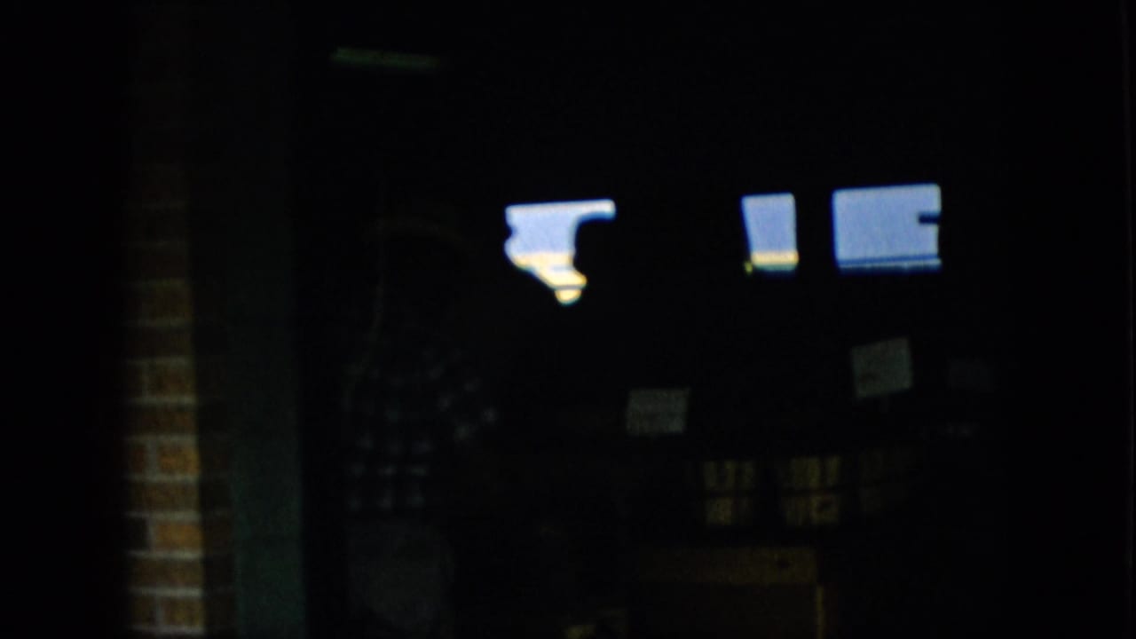 Dim interior view with bright light rectangles, small signs, and a faint figure against the shadows.