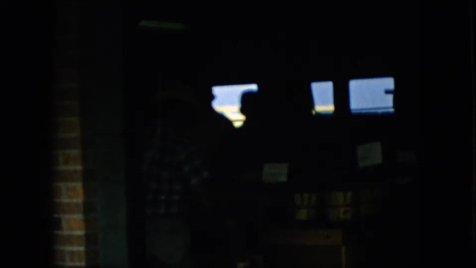 1957 Pennsylvania 8mm frame of a shadowed indoor market view, with bright rectangular light sources near the top and a barely visible person or display area in the darkness.