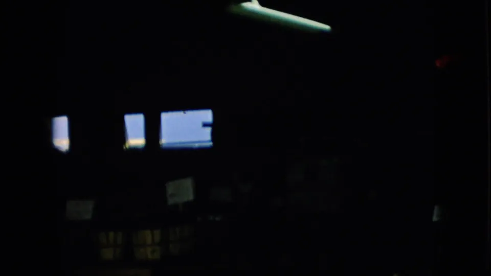1957 Pennsylvania 8mm frame showing an underexposed indoor commercial space, with bright rectangular light at the lower left, small signs, and indistinct market fixtures.
