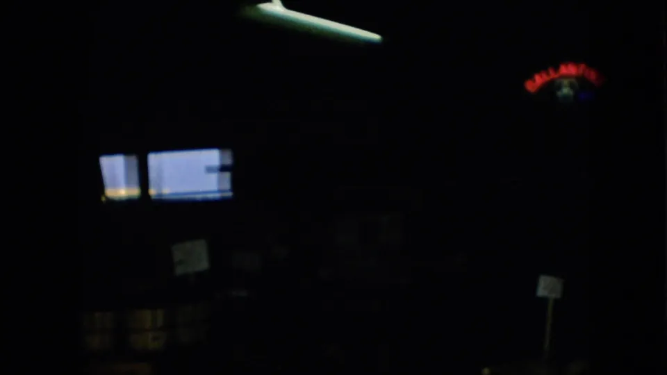 1957 Pennsylvania 8mm frame from a dark market or shop interior, with bright rectangular light shapes, posted signs, and obscured fixtures in heavy shadow.