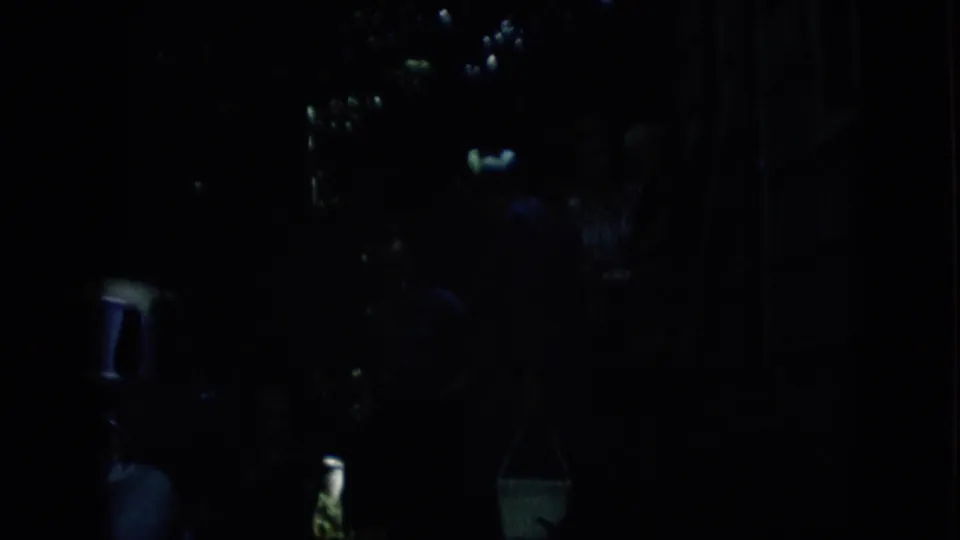 Low-light 1957 Pennsylvania frame with shadowed figures near faint reflections and dark vertical forms, consistent with a brief nighttime home-movie shot.
