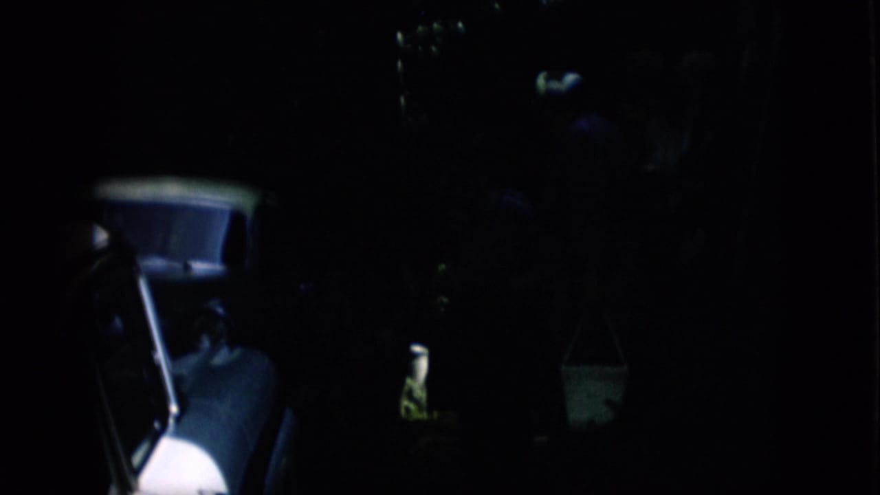 A light-colored car side is more visible beside a dark figure and a hanging bucket.